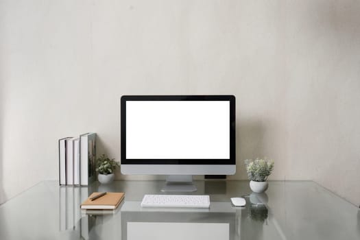 A computer monitor sits on a desk with a keyboard and mouse. The desk is surrounded by books and potted plants. Concept of productivity and organization