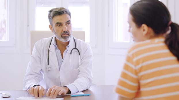 Mature doctor writing while talking with a female patient in a clinic