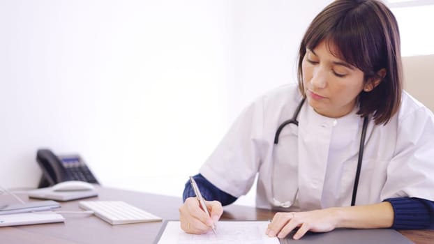 Female doctor filling a medical report sitting on a clinic