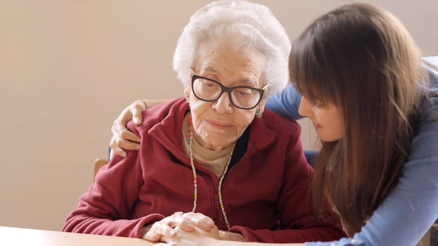 Granddaughter cheers up and hugs her sad grandmother in a nursing home