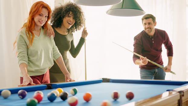 A man performing a good shot in pool and women admiring him