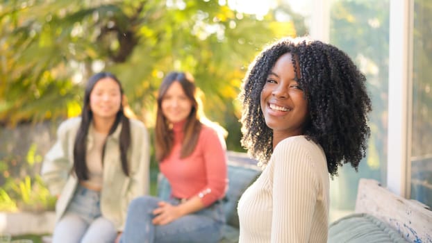 African woman smiling at camera while chatting on the garden with friends in sunset