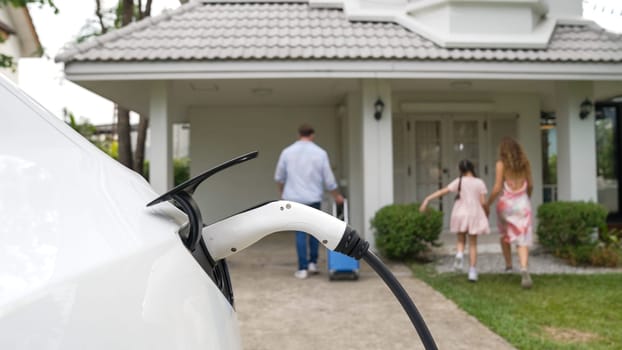 Happy family return from holiday and travel while recharging electric EV car's battery at home charging station. EV car and modern family concept. Synchronos