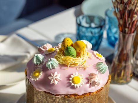 Delicious Easter cake with sugar glaze decorated chocolate eggs and merengue, close up. Festive orthodox easter cake kulich on the table and willow on background