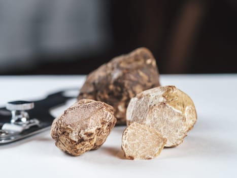 Expensive black truffles gourmet mushrooms on white table in restaurant interior. Row of brown truffles with slice on a white table with dark background. Truffle mushrooms is culinary delight. Close up. Macro.