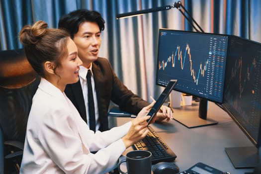 Businesswoman holding tablet on dynamic stock exchange statistic online showing to partners to share, comparing with high or low point graph on computer screen at night neon modern office. Infobahn.