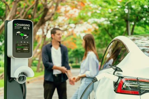 Lovely young couple recharging battery for electric car during autumnal road trip travel EV car in autumnal forest. Eco friendly travel on vacation during autumn. Exalt