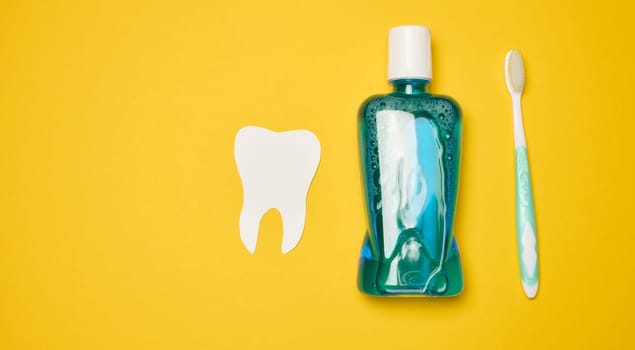 Mouthwash and toothbrush on yellow background, top view