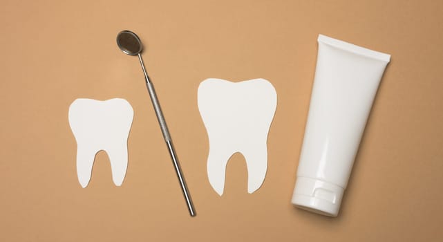 Tube with toothpaste and dental mirror on a brown background, oral hygiene