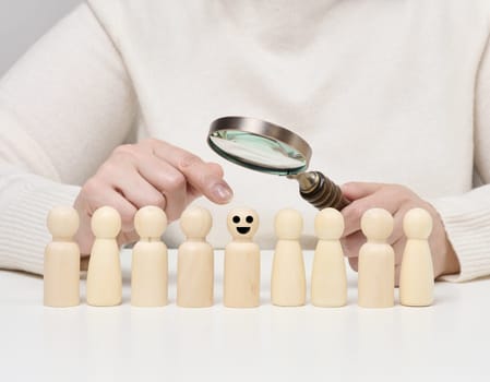 Woman holding a magnifying glass and wooden men on a white table. Personnel recruitment concept, talented employees. Career advancement