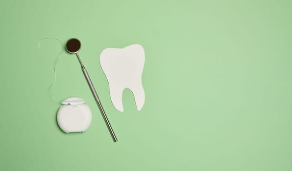 Dental floss and paper teeth on green background, oral hygiene, top view