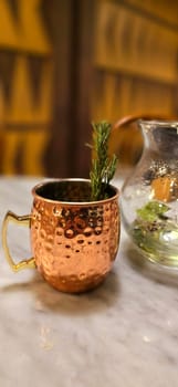 Traditional iced tea served in a unique and artistic brass cup , ice tea garnished with rosemary twigs in a restaurant