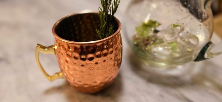 Traditional iced tea served in a unique and artistic brass cup , ice tea garnished with rosemary twigs in a restaurant