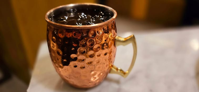 Traditional iced tea served in a unique and artistic brass cup , ice tea garnished with rosemary twigs in a restaurant
