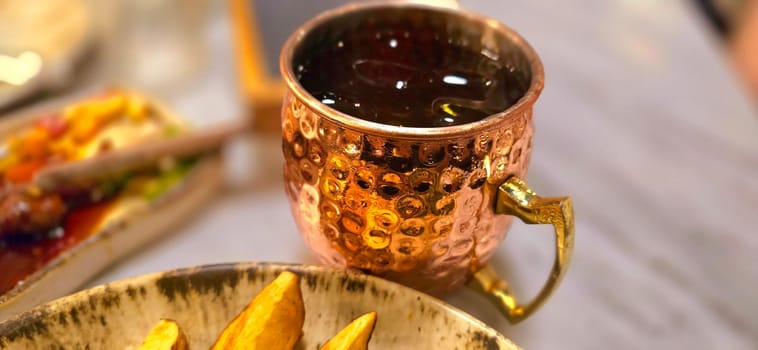 Traditional iced tea served in a unique and artistic brass cup , ice tea garnished with rosemary twigs in a restaurant