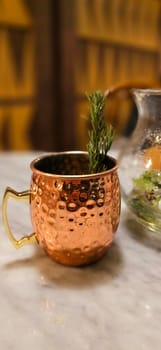 Traditional iced tea served in a unique and artistic brass cup , ice tea garnished with rosemary twigs in a restaurant