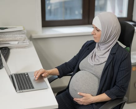 Pregnant Caucasian woman in hijab working at a computer in the office