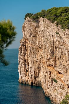 Sheer cliffs with green trees, rocky wall by sea on summer sunny day in Dugi Otok island, Telascica National Park, Croatia