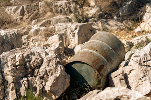 Metal rusty barrel on rocky beach, environmental pollution with garbage and old oil tank