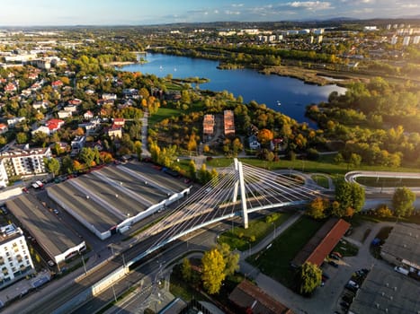 Drone perspective view of modern bridge, Bagry bay and city park in Krakow, Poland. Summer overhead scene of suspension bridge with steel cables and buildings on Saska street, blue water of pond