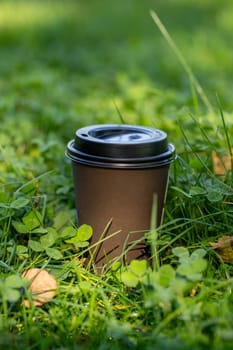 Brown paper cup with hot breakfast coffee on summer bright green grass of city park or garden