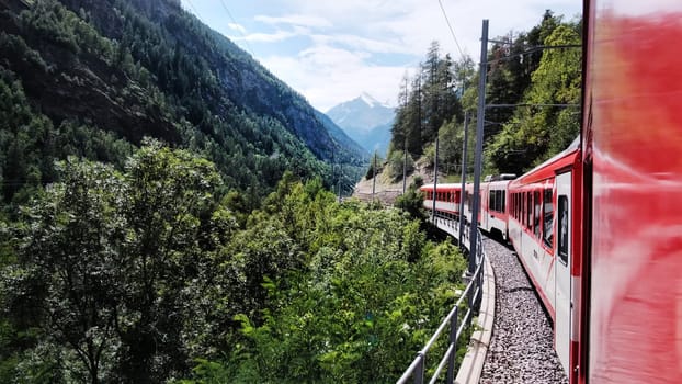 Red Swiss Train Moving By Valley In Mountains In Switzerland