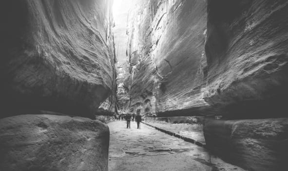 Tourists walking at amazing huge rocky canyon near Petra in Jordan. Black and white photo.