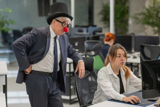 Caucasian woman works at the computer. Elderly man in clown costume in office