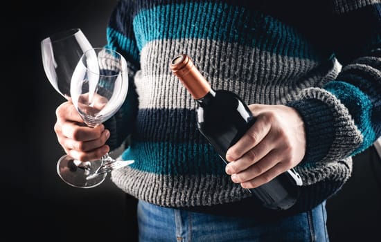 Man holding wine bottle and glasses closeup on black background. Guy with grape alcohol beverage and wineglasses