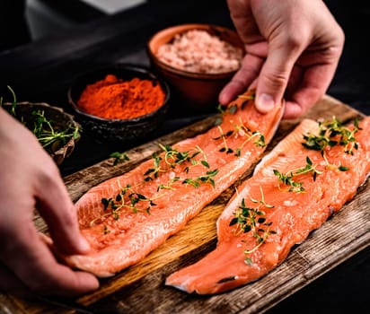Chief hands put fresh trout salmon filet with herbs on wooden board. Omega orange fish with rosemary for healthy nutrition