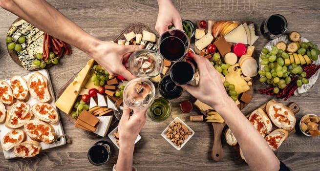 People hands with wine glasses, grape and variety of cheese kinnds. Delicatessen food collection with alcohol beverage