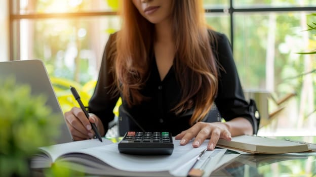 A woman is sitting at a desk with a calculator and a pen. She is writing something down in a notebook