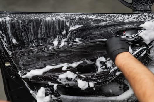 A man cleans the interior of a car with foam and a brush. Clean the door trim