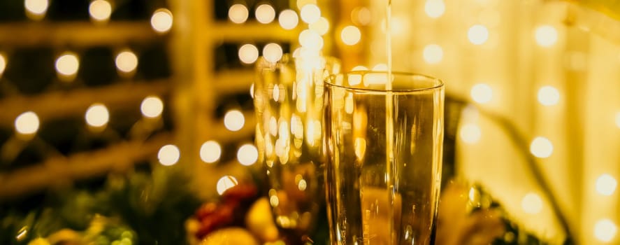 Two champagne glasses filled with champagne are placed on a table with a fruit arrangement. The glasses are surrounded by lights, creating a festive atmosphere. The table is set for a celebration or a special occasion