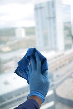 hand in blue glove cleaning window with green rag.