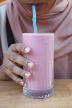 a woman sipping a pink milkshake from a cup with a straw