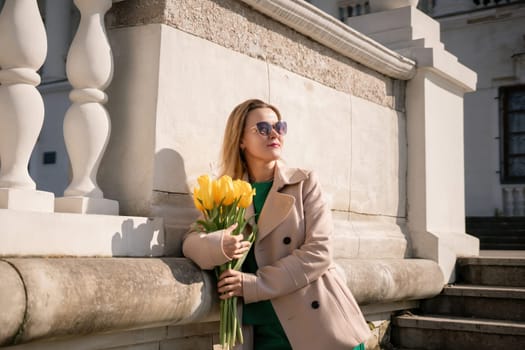 Woman holding yellow tulips, leaning against stone wall. Women's holiday concept, giving flowers