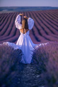 Back view woman lavender sunset. Happy woman in white dress holds lavender bouquet. Aromatherapy concept, lavender oil, photo session in lavender.