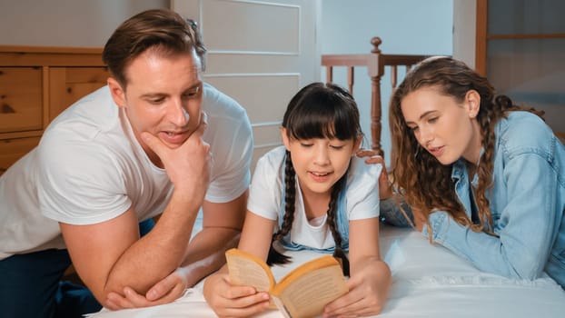 Bedtime story with childhood storytelling, mom and dad reading a fantasy book together to their little young girl in cozy and comfortable bedroom. Modern family happy time. Panorama Synchronos