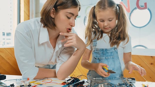 Young smart caucasian teacher teaching students about part of electronic board. Expert girl learn about digital electrical tool and fixing motherboard at table with chips and wires placed. Erudition.