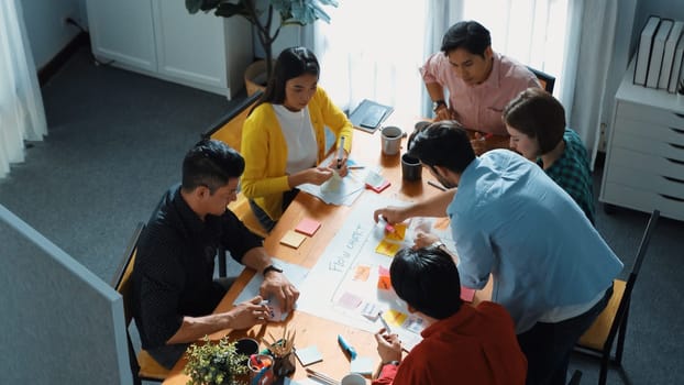 Top down view of diverse people brainstorming and making scrum task board. Group of skilled business team working together and writing sticky notes to share plan and using kanban board. Convocation.