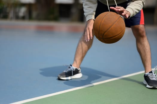 Cropped shot of basketball player bouncing the ball on an outdoor court during a sunny day.