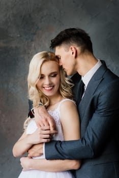 Cute wedding couple in the interior of a classic studio. They kiss and hug each other.