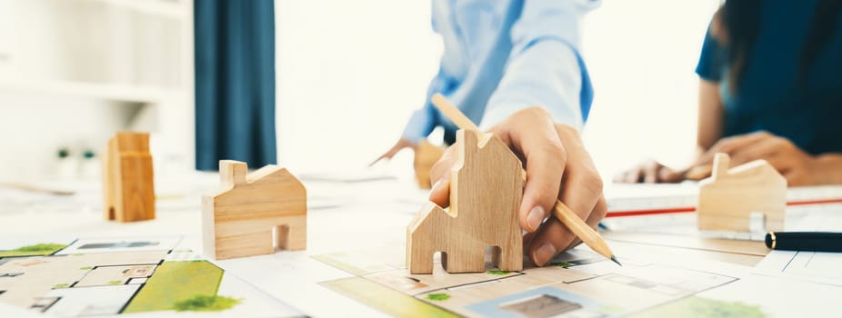 Professional architect engineer team discussion about architectural project on meeting table with wooden block and blueprint scatter around. Design and cooperate concept. Closeup. Delineation.