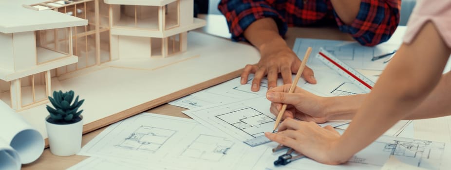 Architect team analysis and brainstorming about house construction at meeting table with house model, blueprint and architectural equipment scatter around. Creative design and teamwork. Burgeoning.