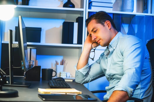 Working businessman sleepy feeling with project at night time, waiting email information sending back at modern workplace. Theme of freelancer tired of remote online work in over time. Sellable.