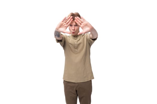 young caucasian guy dressed in khaki short sleeve shirt shows stop gesture.