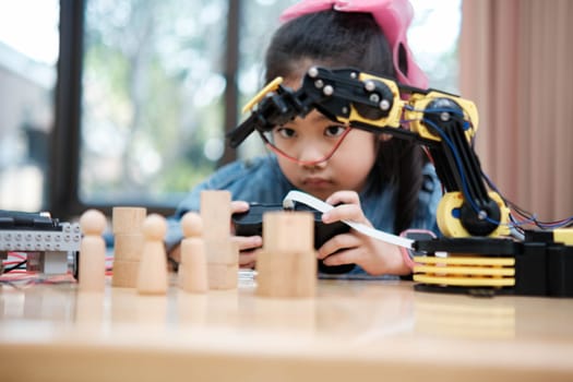 A primary school girl focuses on operating a robotic arm with a remote control, demonstrating STEM education in action.