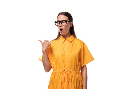 european young brunette lady dressed in an orange summer dress and glasses points her finger to the side in surprise.