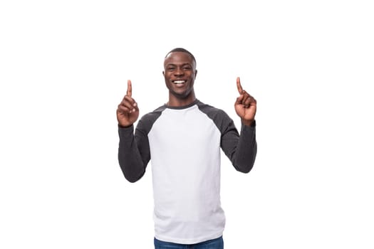 young joyful african guy dressed in a black and white sweatshirt and jeans on a white background with copy space.